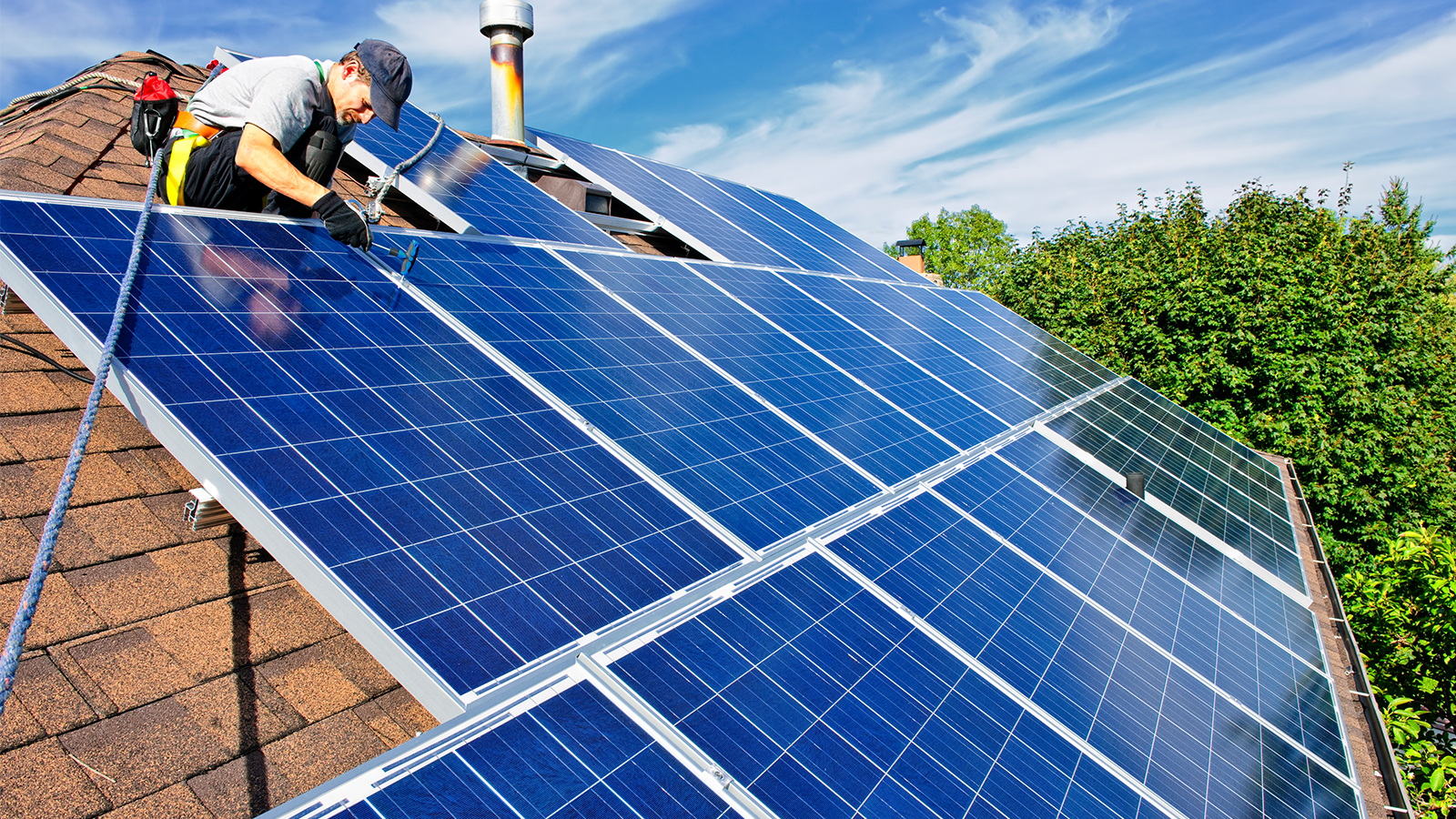 A solar expert installs new solar panels on a home's roof on a sunny day.