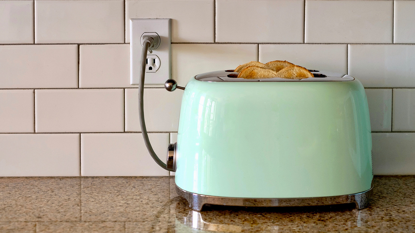 A green toaster on a kitchen countertop plugged into an electric outlet.
