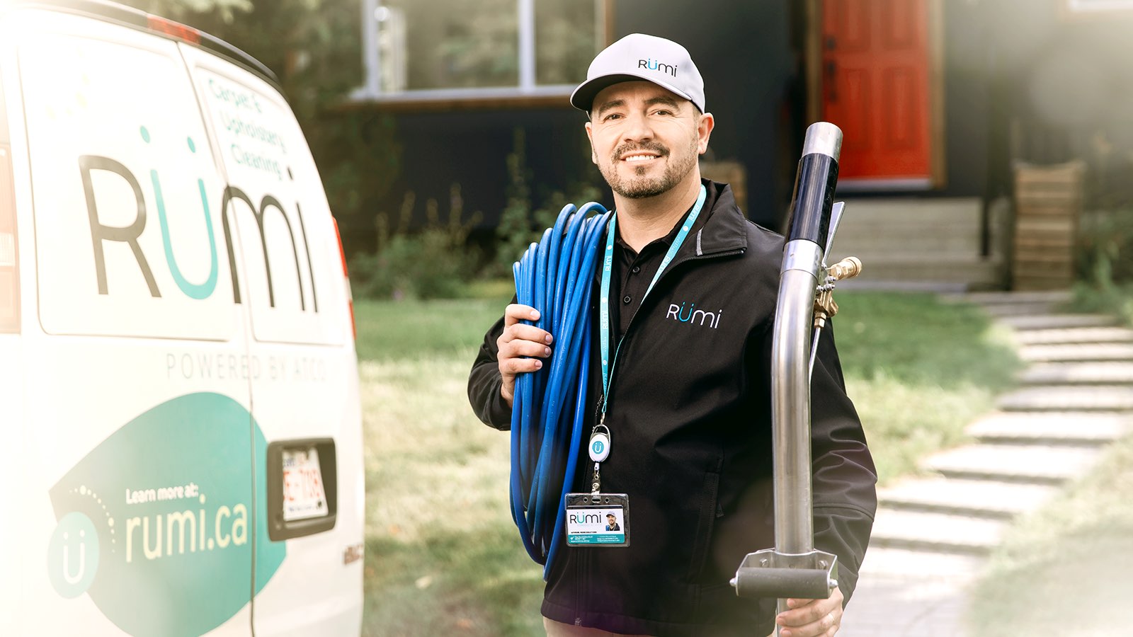 A Rümi technician smiling and facing forward outside beside Rümi work van carrying equipment for home services. 